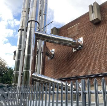 Silver pipes going into a brick building for heating