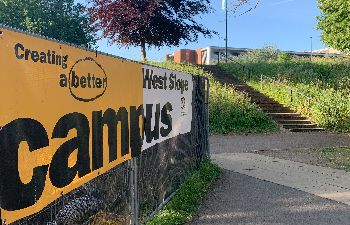 An image of a pathway with a yellow and white 'Creating a Better Campus' banner to the side