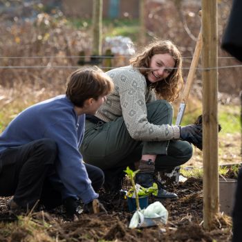 Two young females smile at each other while kneeling down to plant