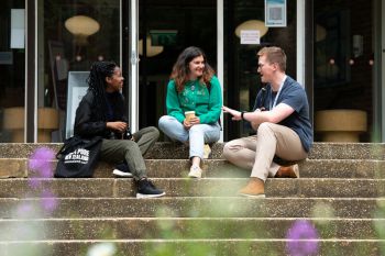 Three smiling people sat in the entrance steps having a conversation