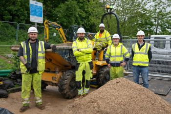 Five colleagues in hi-vis on a site where cabling has been dug up.